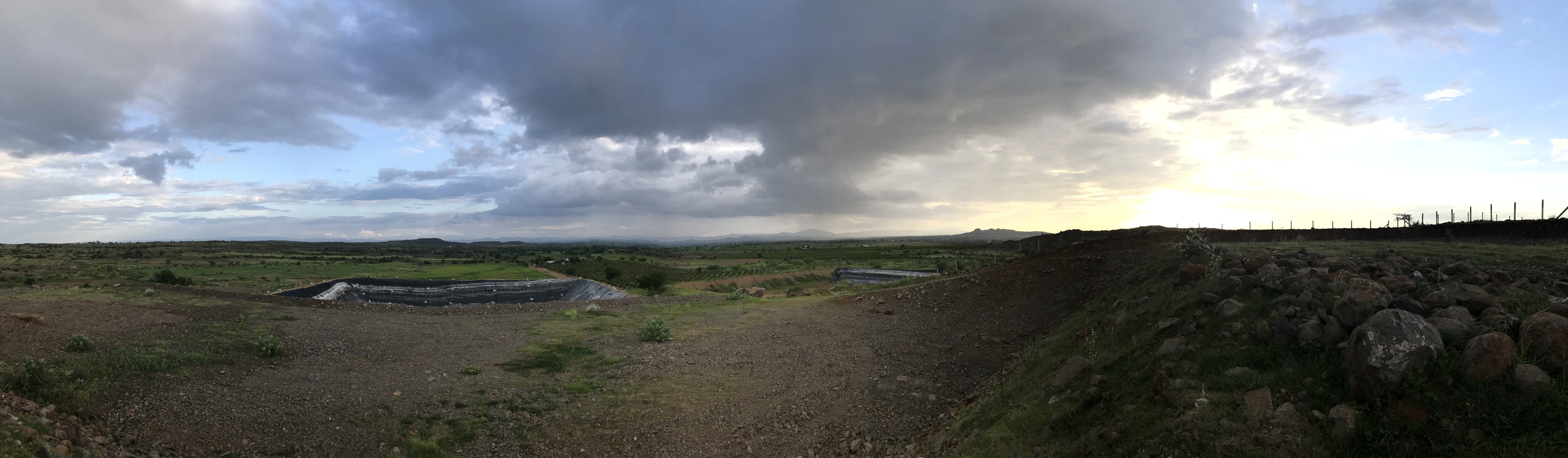 A wide panorama of the farm, the pond and the hills under evening clouds